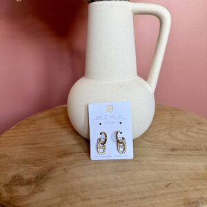 "Boucles d'oreilles créoles dorées en acier inoxydable avec pendentif maillon de chaîne pavé de strass, présentées par Milë Mila sur un support en bois."