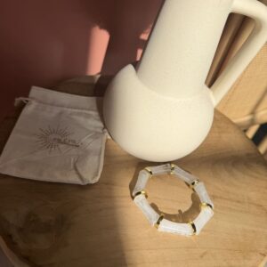 Bracelet élastique Milémila composé de segments facettés en résine effet pierre blanche (type quartz ou marbre) et d'inserts dorés, présenté avec son pochon sur une table en bois clair.