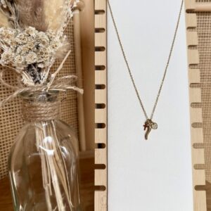 Collier fin doré avec pendentifs mini piment, croix et cœur serti de strass sur présentoir en bois.