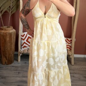Femme portant la robe longue Goa Fio jaune pastel à fleurs blanches, coupe évasée et décolleté en V.