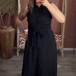 Robe longue noire sans manches avec ceinture nouée portée par une femme devant un décor bohème en tons terracotta