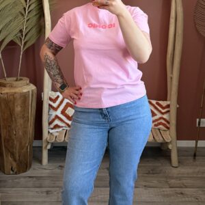 Zoom sur un jean droit bleu clair délavé porté avec des sandales beiges à boucles dorées et un t-shirt rose.