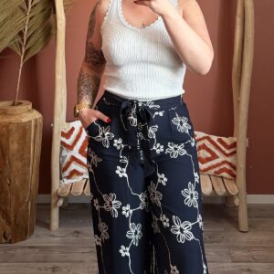 Débardeur blanc à encolure festonnée porté avec un pantalon large bleu marine à imprimé fleurs blanches.