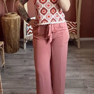 Top sans manches en maille crochet à motifs géométriques orangés et roses, porté avec un pantalon large assorti.